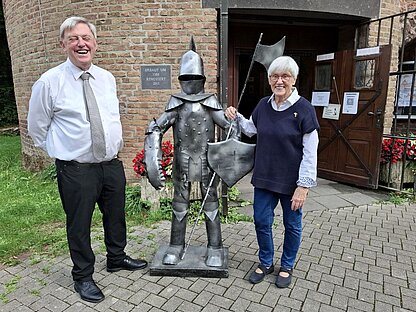 Pfarrer Paul Hauser und Pastorin Ortrun Hindemith zwischen dem eisernen Burgknappen vor der Burg Uda in Oedt. Burgdienst_Pfarrer_small